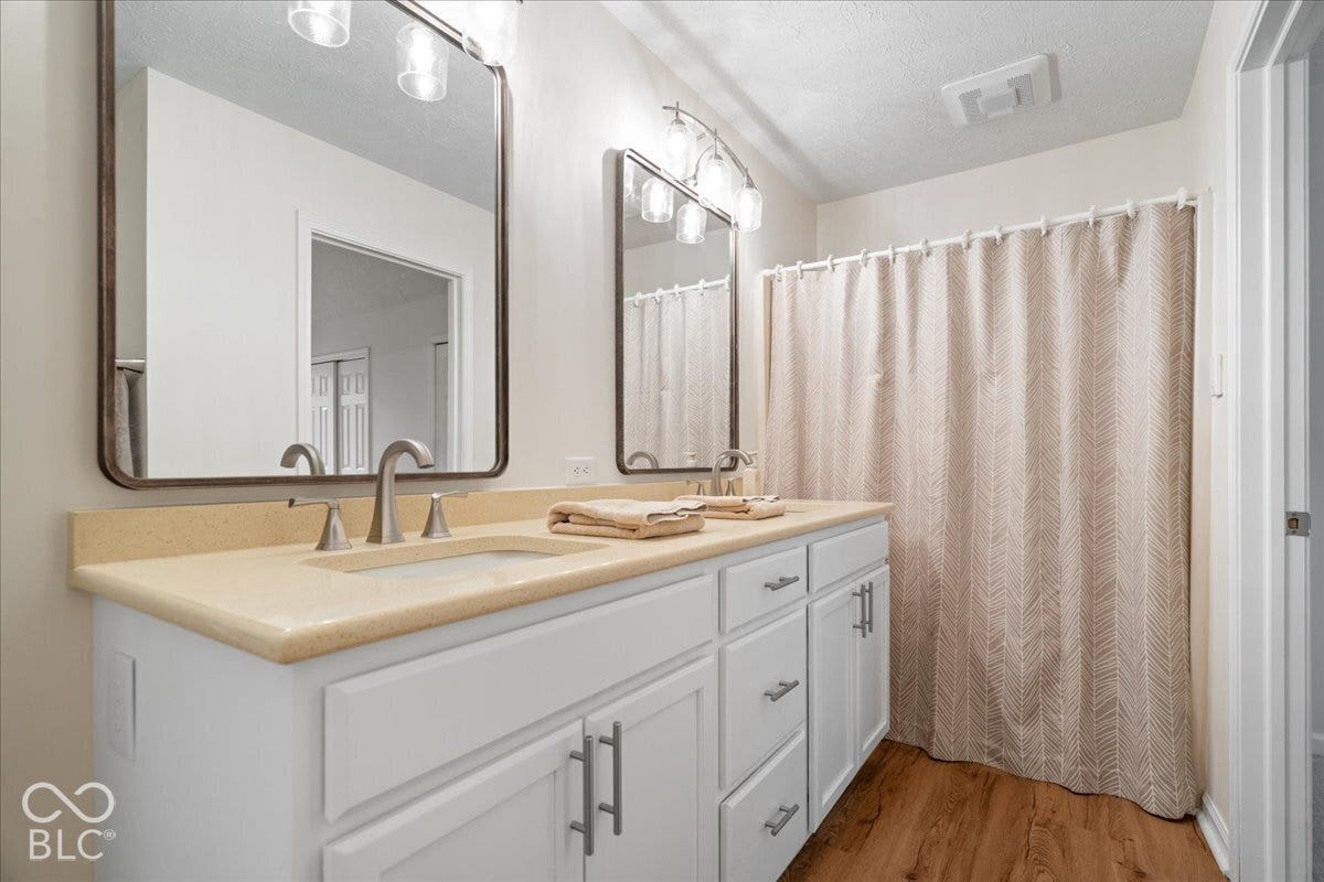 Upstairs hall bath that also opens to bedroom. Dual-sink vanity with a solid surface countertop, rectangular undermount basins, brushed nickel hardware, and two framed mirrors with integrated multi-light fixtures