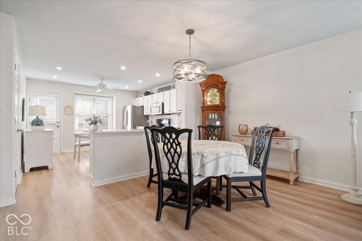Open-concept interior featuring light wood-finish flooring, recessed lighting, white cabinetry, a kitchen peninsula, and a multi-light drum pendant fixture