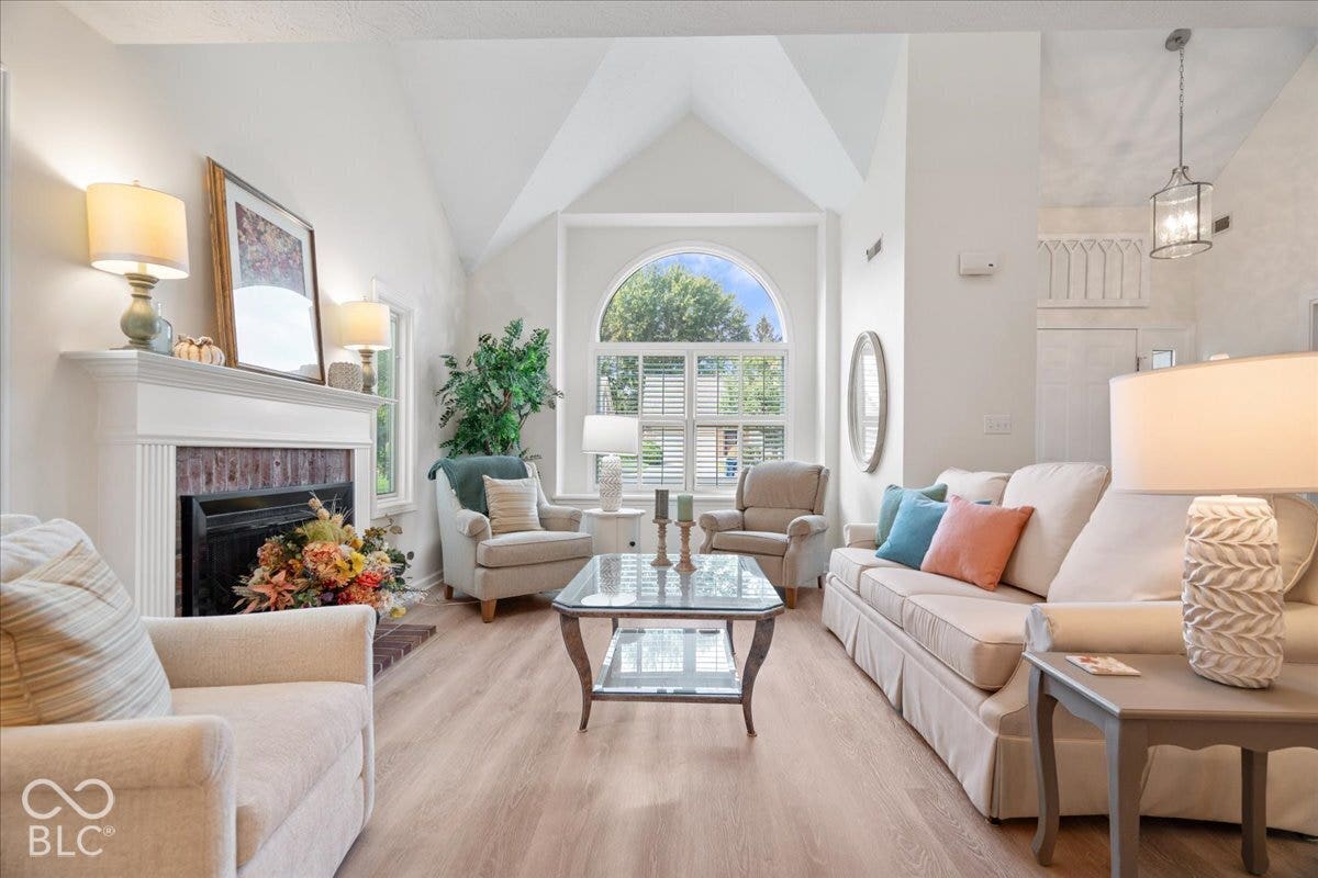Vaulted ceiling, brick-surround fireplace with a classic mantel, arched window, and wood-finish flooring