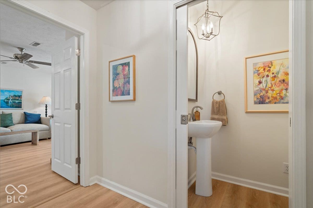 Powder room featuring a porcelain pedestal sink, arched wall mirror, and an iron-frame lantern-style pendant light, accented by laminate wood-finish flooring