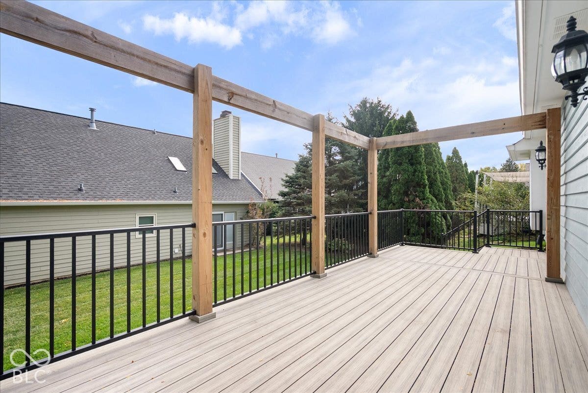 Raised deck featuring composite decking, vertical wood-post pergola, black metal railing, and wall-mounted exterior lanterns