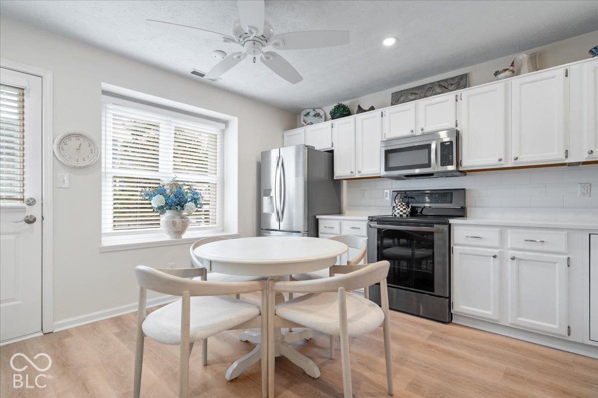 Kitchen featuring white cabinetry, subway tile backsplash, stainless steel appliances, wood-finish flooring, and a large window