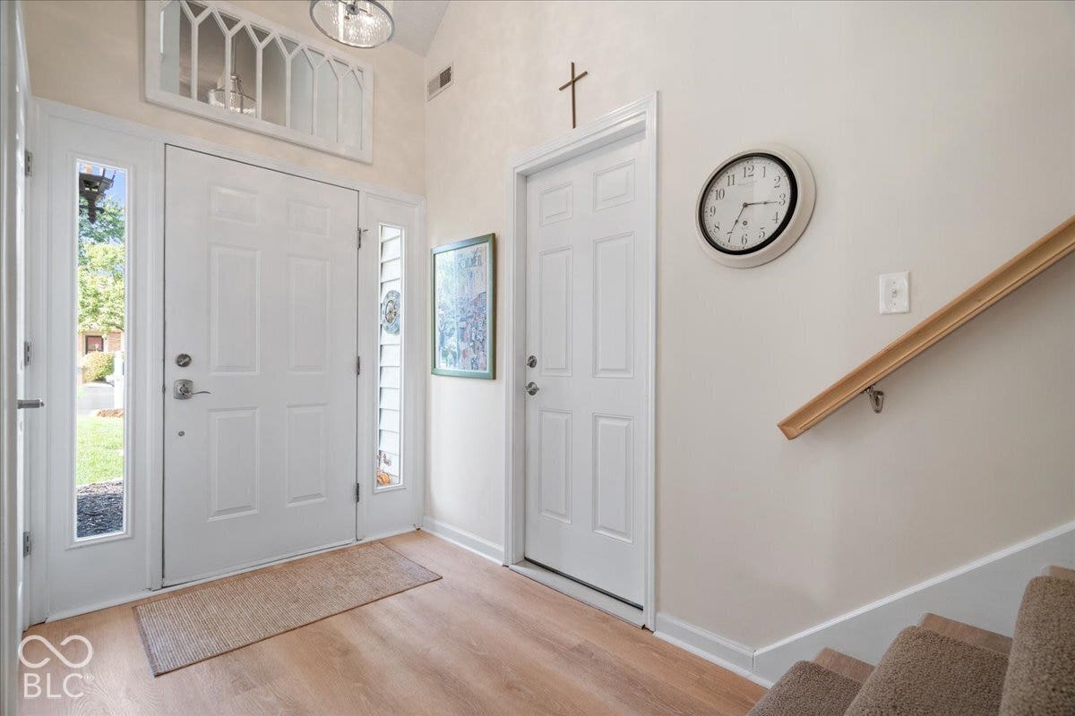 Entryway featuring a solid door with flanking glass sidelights, transom window, wood-finish flooring, and a wall-mounted wooden handrail