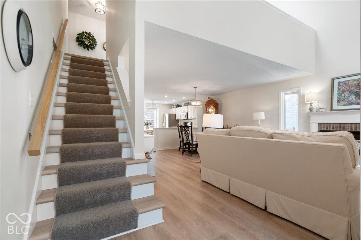 Staircase with carpeted treads and wood-finish handrail, vaulted ceiling, wood-finish flooring, and a fireplace with a mantel