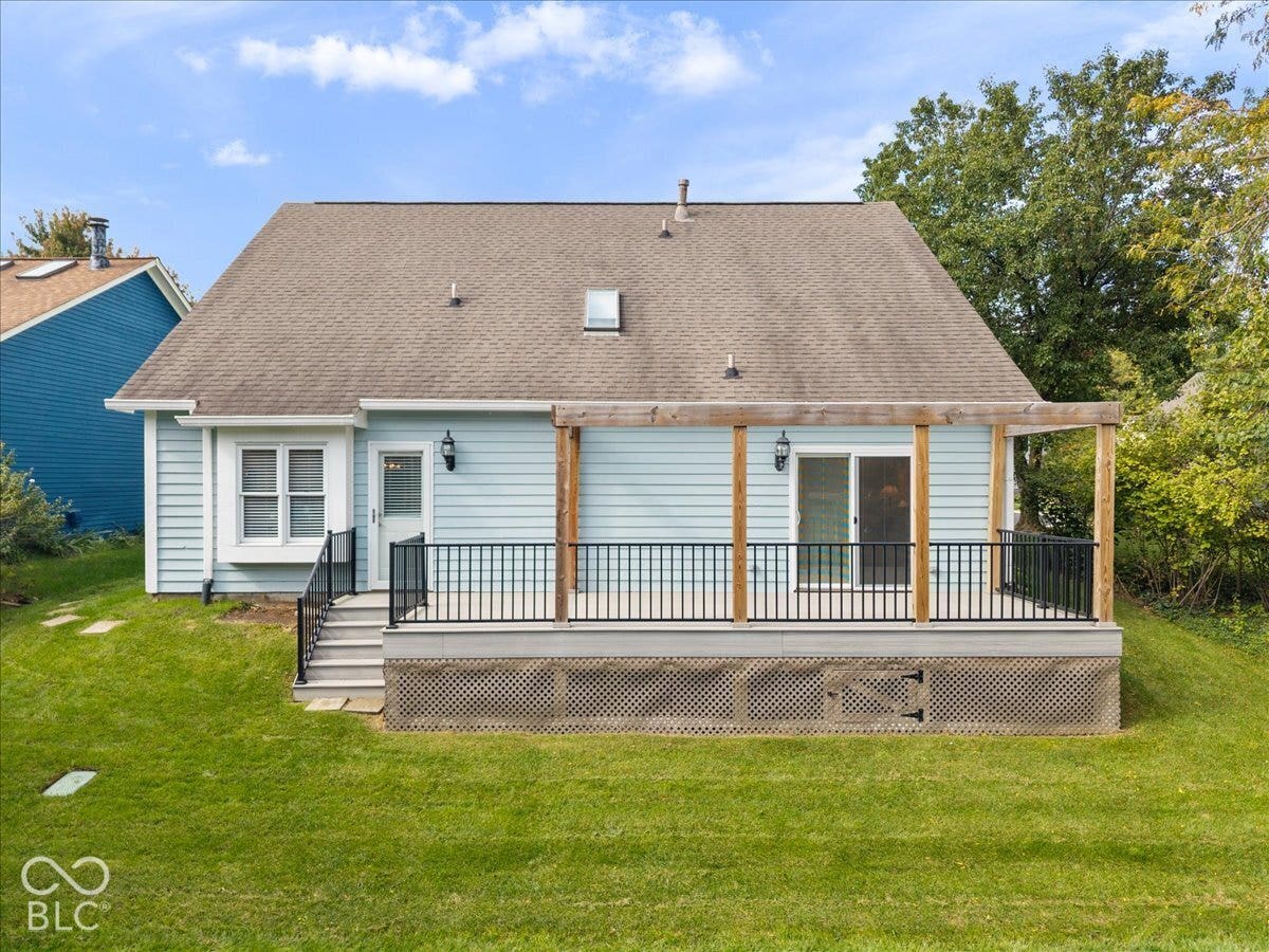 Rear exterior featuring light blue horizontal siding, an expansive composite deck with a timber pergola, black metal railings, and lattice skirting