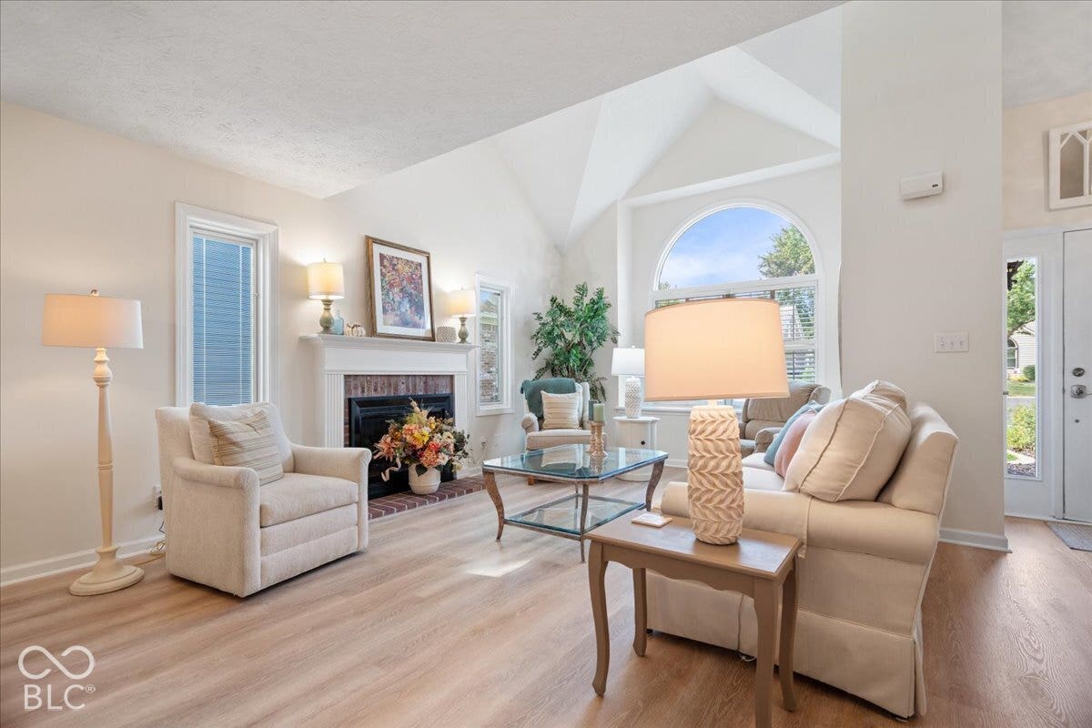 Vaulted ceiling, arched window, wood-finish flooring, and fireplace with a decorative mantel