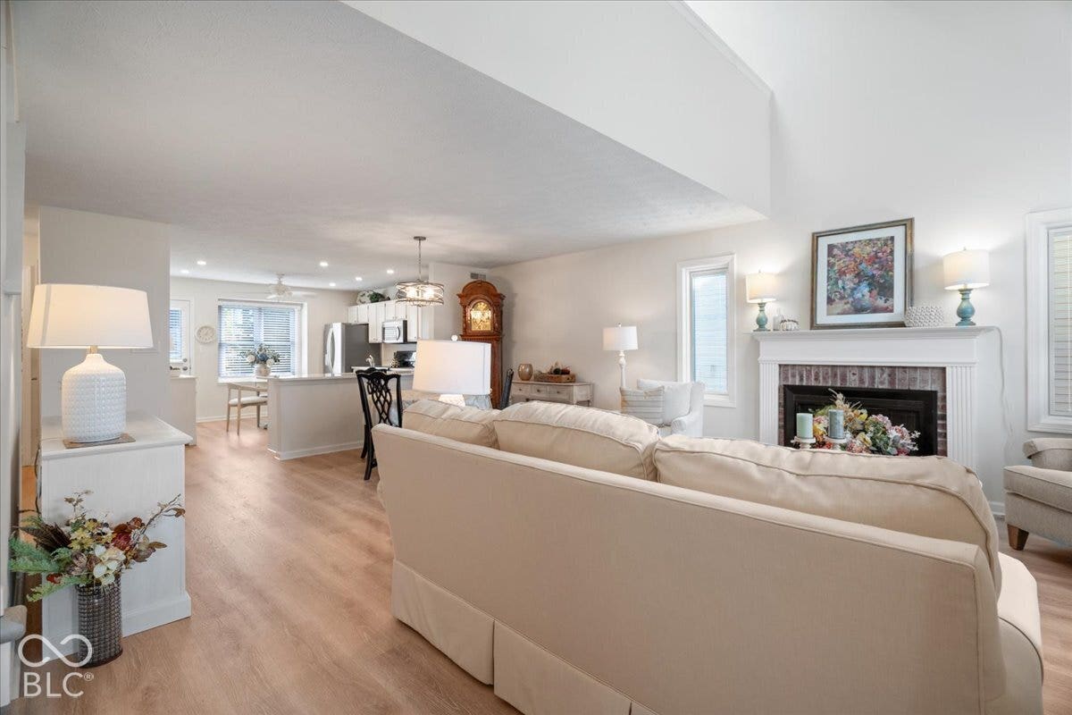 Open-concept interior featuring vaulted ceilings, wood-finish flooring, a brick-surround fireplace with a mantel, recessed lighting, and a kitchen peninsula