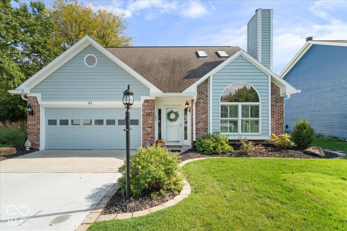 Exterior featuring light blue lap siding, brick facade accents, a multi-paneled garage door, roofline skylights, and a prominent chimney stack