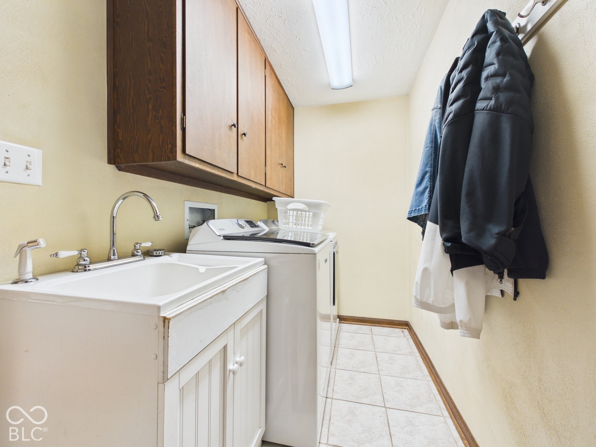 Laundry area featuring wood-finish cabinetry, a utility sink with dual-handle faucet, ceramic tile flooring, and a fluorescent ceiling light