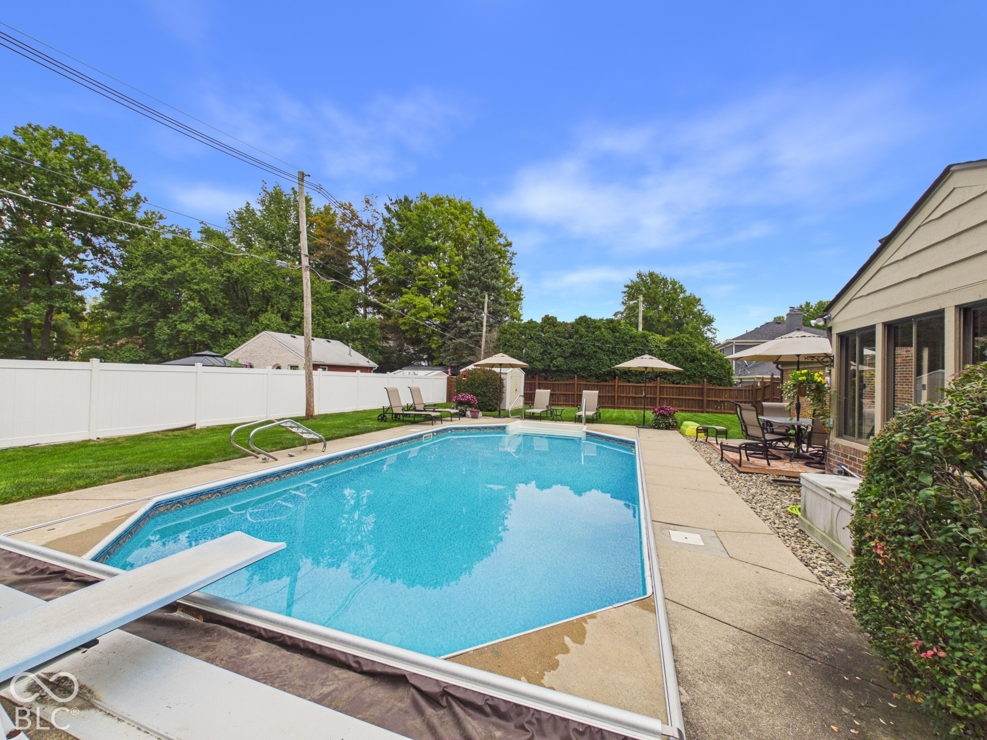 In-ground swimming pool with diving board, concrete surround, and privacy fencing