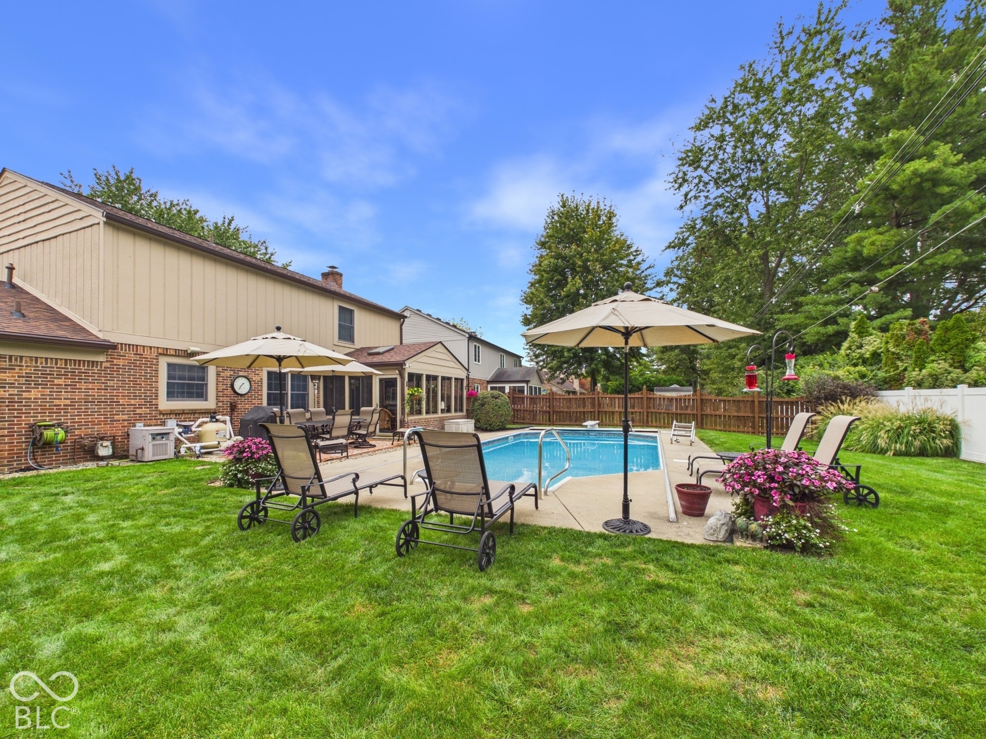Expansive green lawn, in-ground swimming pool, concrete patio, brick exterior, and wood fencing