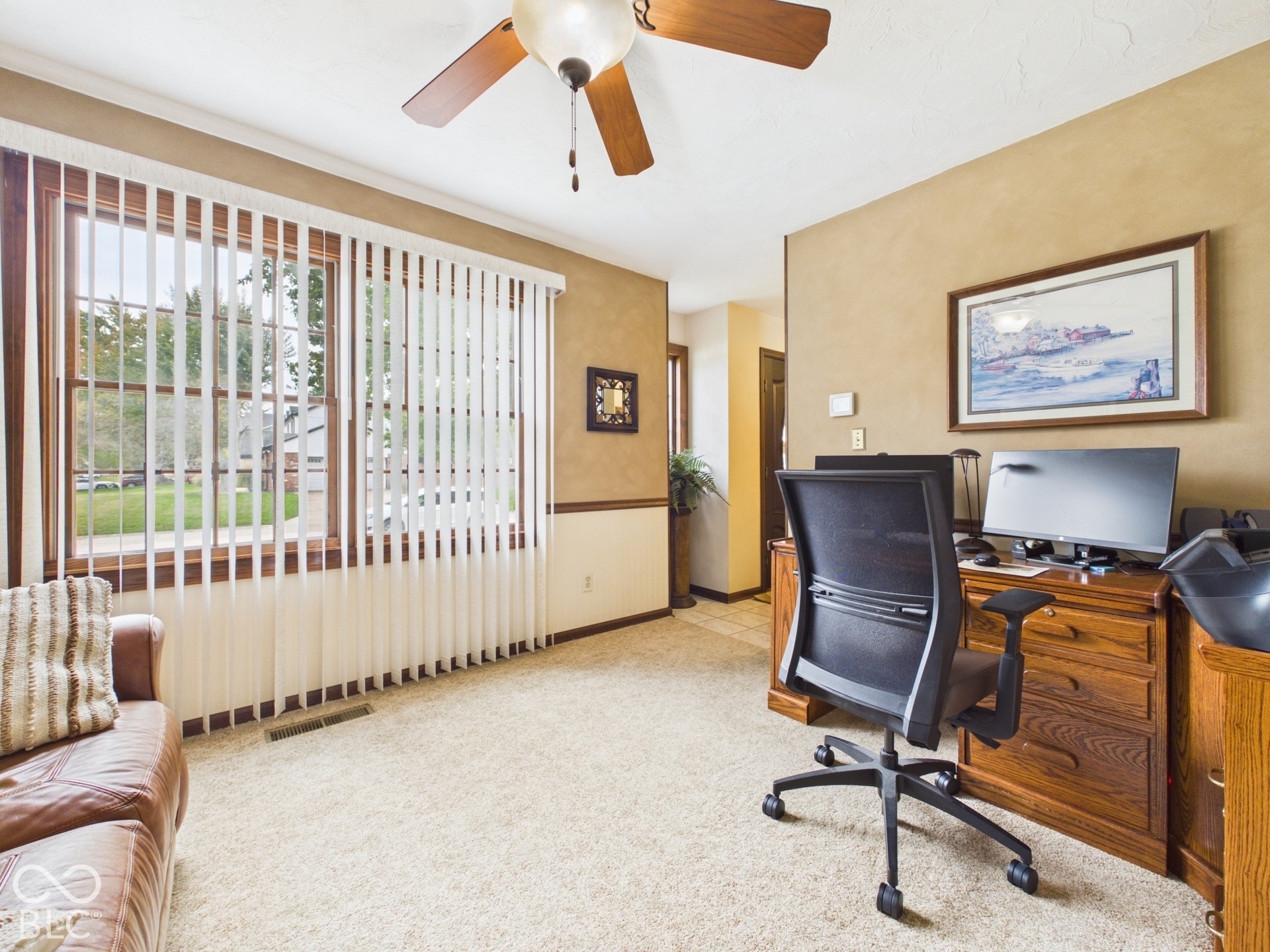 Expansive window with vertical blinds, ceiling fan with integrated lighting, two-tone wall treatment with chair rail, and soft carpet flooring