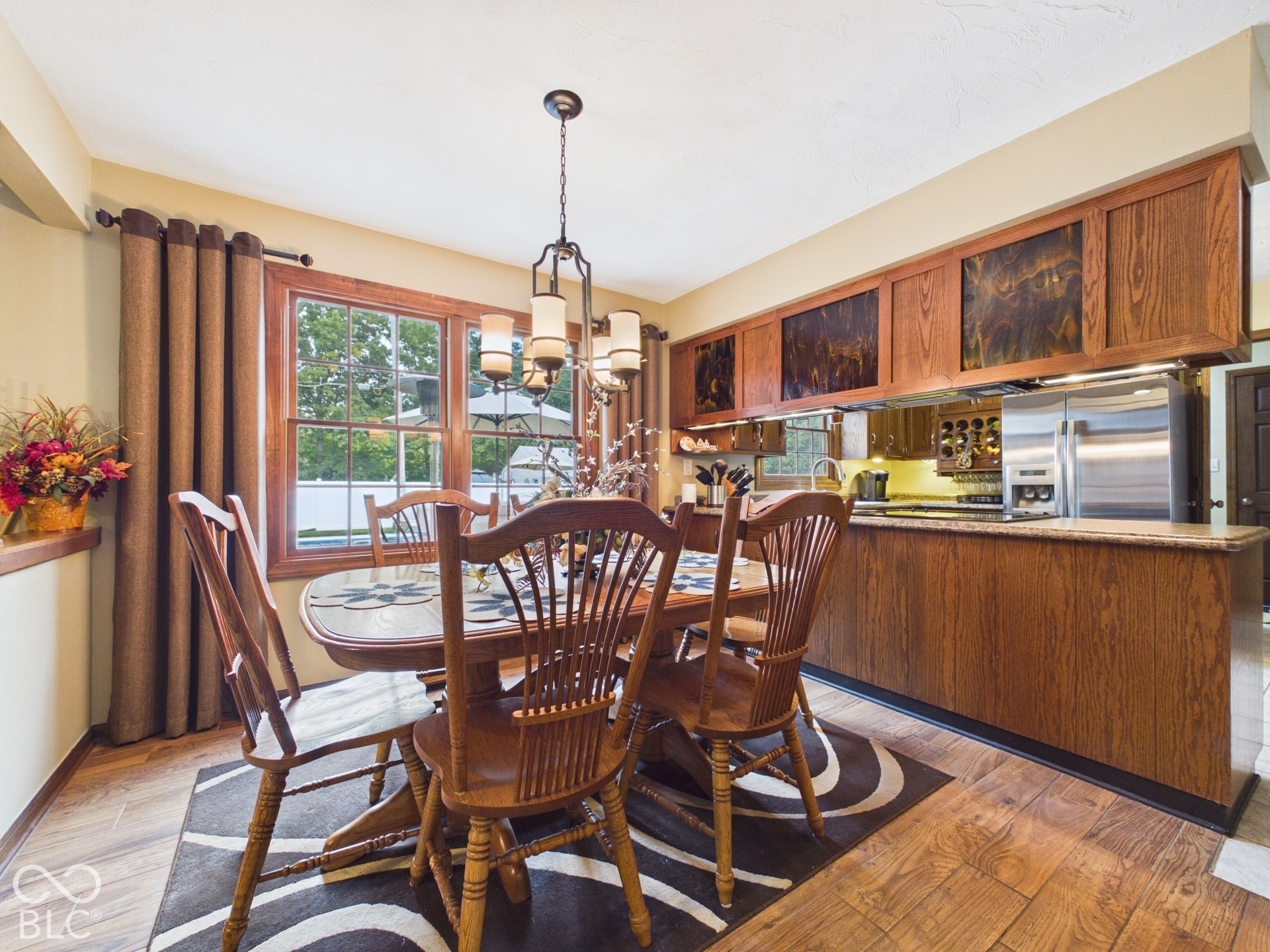 Wood-finish flooring, recessed ceiling lighting, and a chandelier illuminate this dining area with a window overlooking exterior landscaping