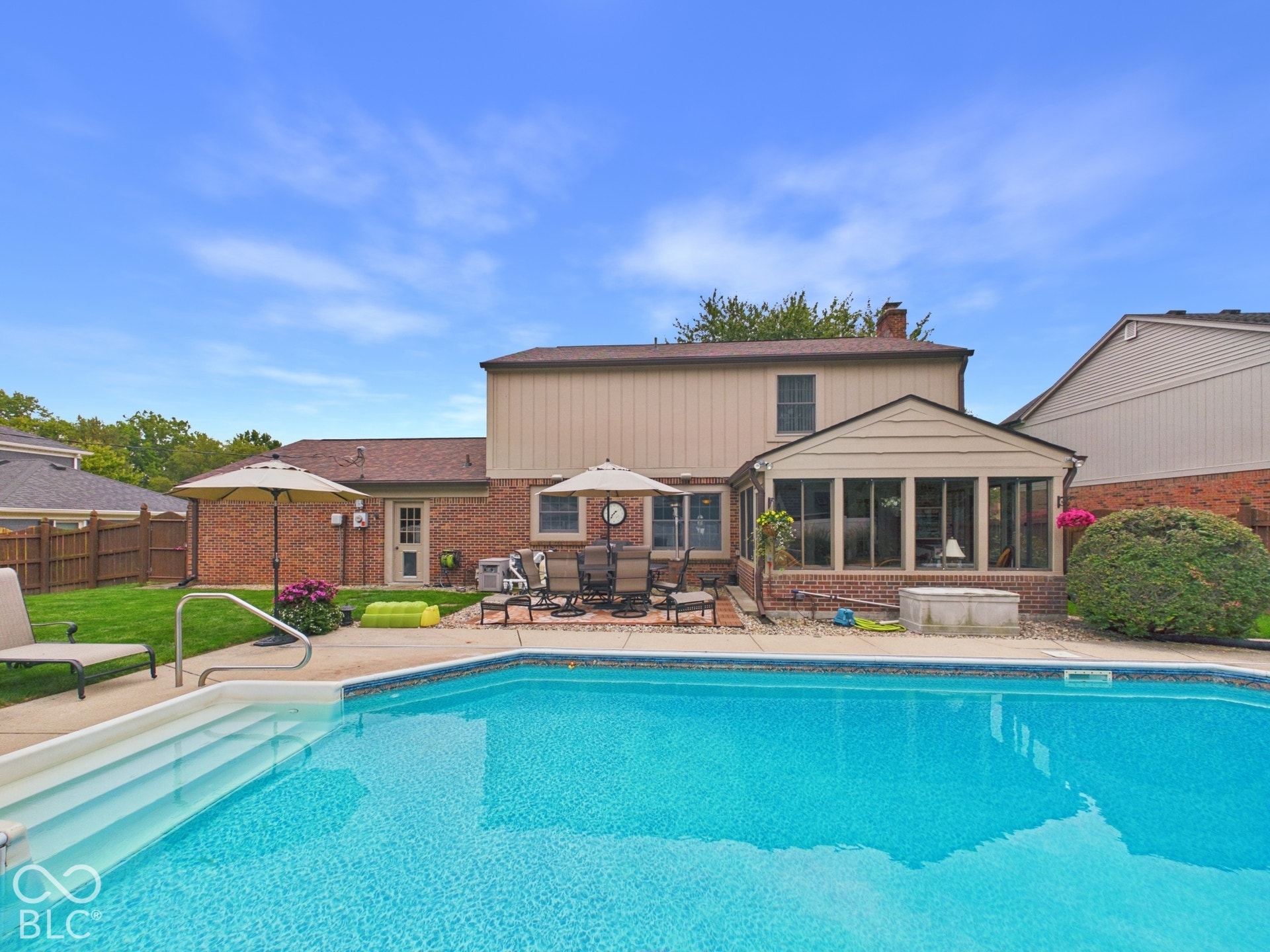 Backyard featuring a built-in swimming pool with steps, a paver patio, an enclosed sunroom, and a brick and siding exterior