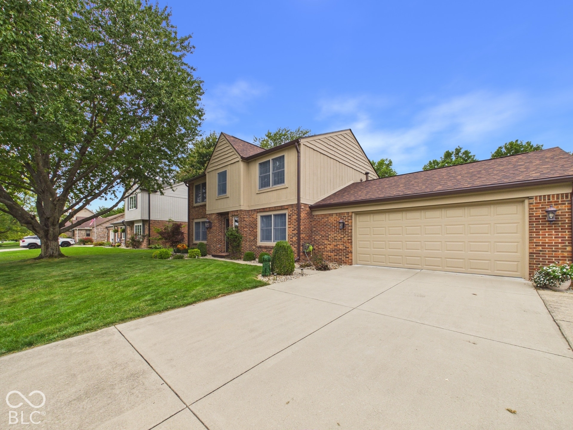 Two-story exterior with a brick and siding facade, attached two-car garage, concrete driveway, and established landscaping