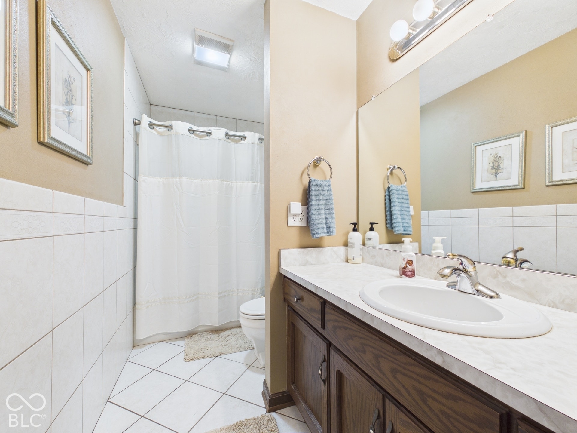 Bathroom featuring a vanity with dark wood-finish cabinetry, a large mirror, and a full tile-surround shower with white tiling