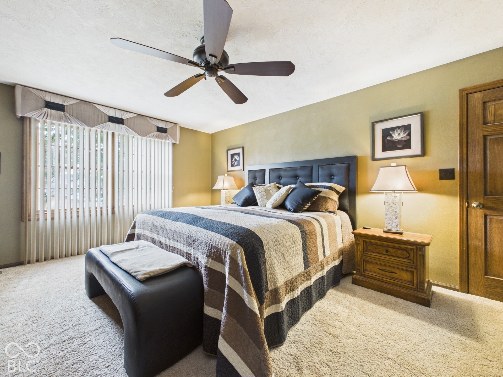 Ceiling fan with integrated lighting, wood-finish door, textured wall finish, window with vertical blinds and valance, and wall-to-wall carpeting