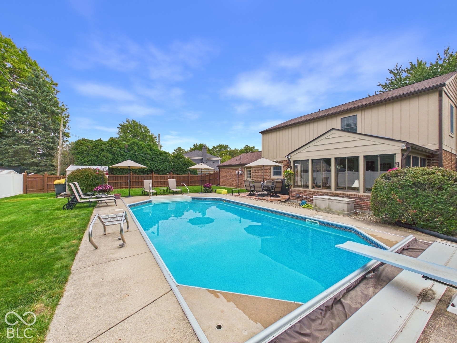 In-ground swimming pool with diving board, concrete surround, and a fenced yard