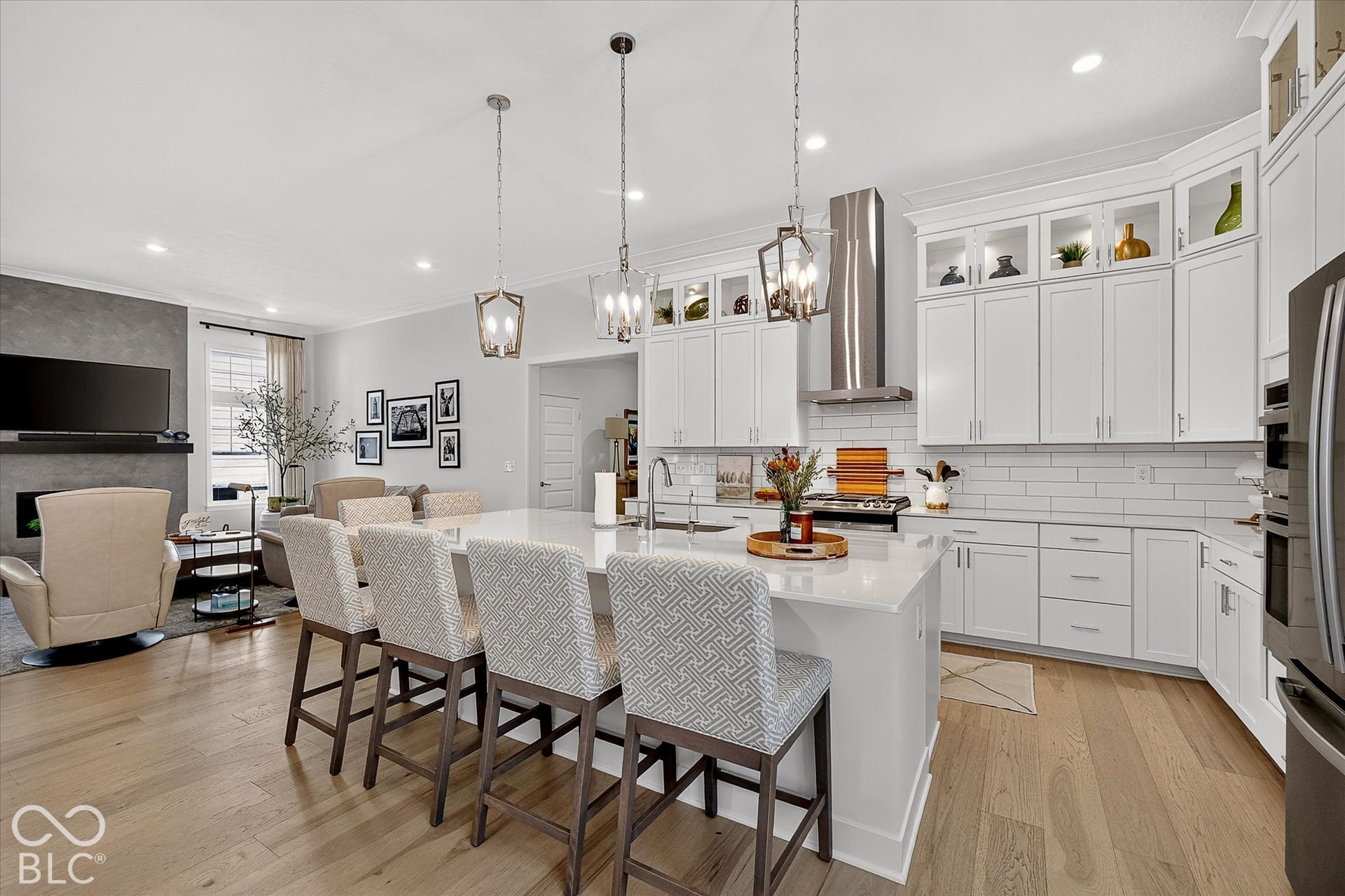 1405 Lake Haven Lane, Westfield, IN 46074 Open-concept living space featuring wood-finish flooring, a kitchen island with seating, pendant lighting, white cabinetry with glass-front uppers, and a stainless steel range hood