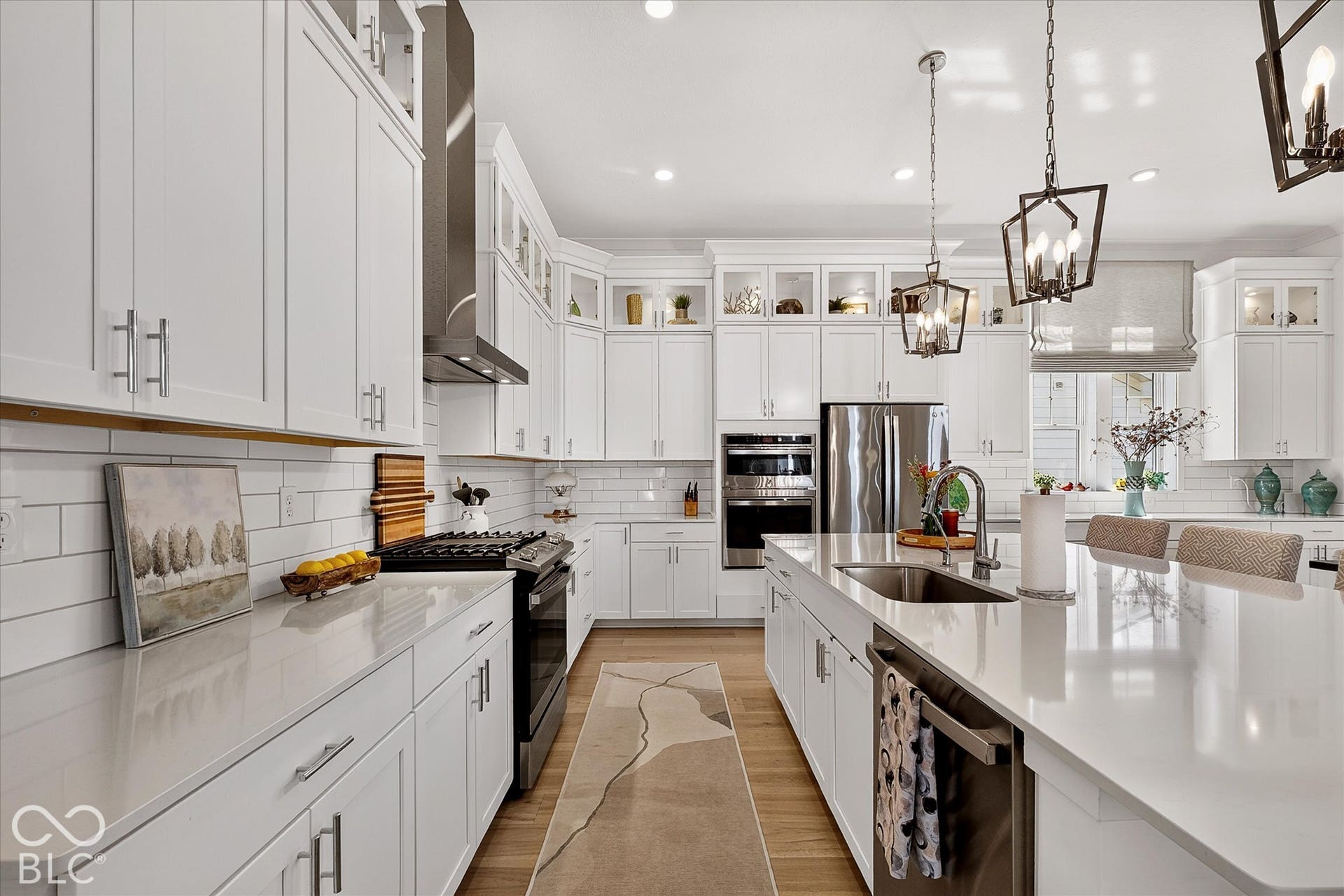 1405 Lake Haven Lane, Westfield, IN 46074 White shaker cabinetry, stainless steel appliances, central kitchen island with undermount sink, subway tile backsplash, and wood-finish flooring