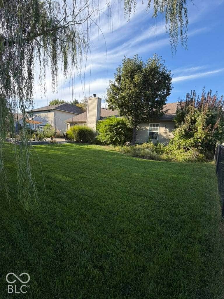 Expansive lawn area with mature trees and shrubbery, featuring a visible chimney structure and a residential building with exterior siding