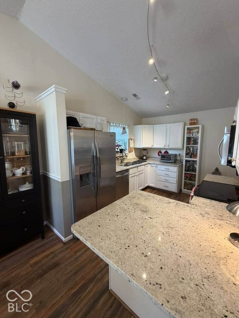 Kitchen with granite-look countertops, stainless steel appliances, wood-finish flooring, white cabinetry, and vaulted ceilings