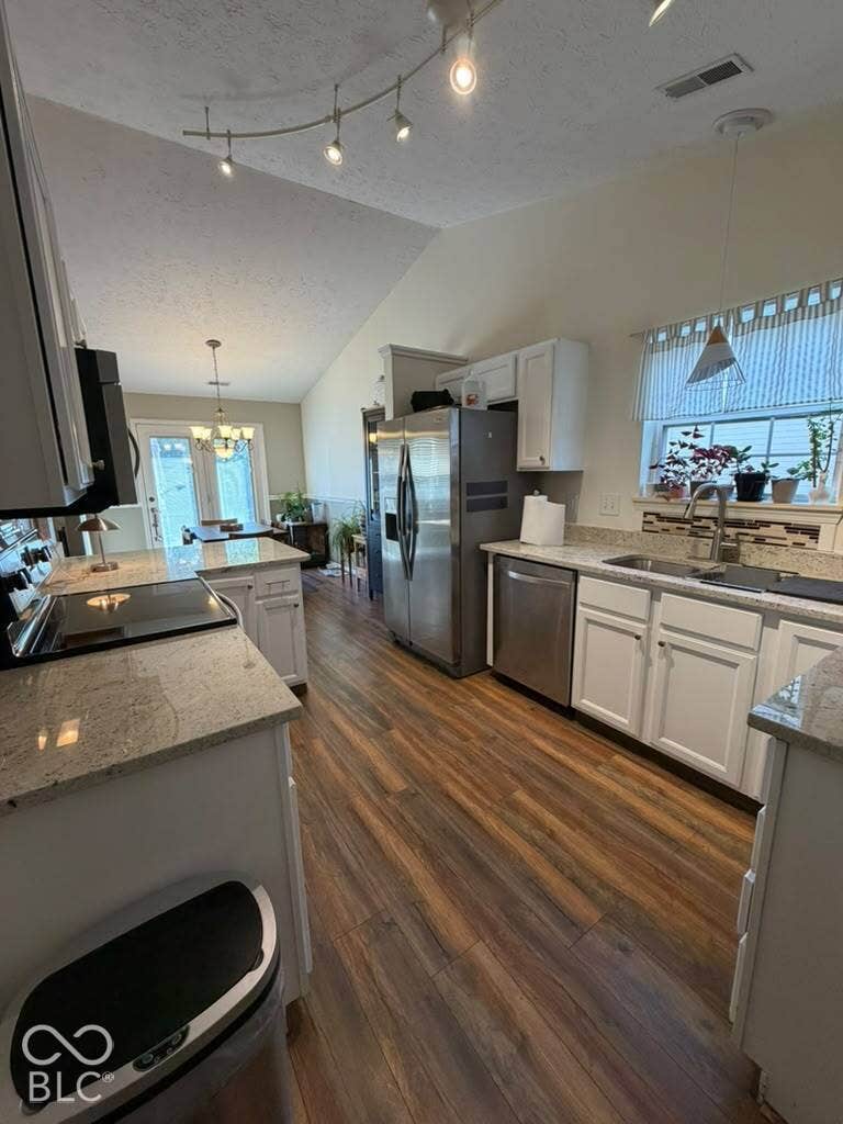 Vaulted ceiling, track lighting, wood-finish flooring, white cabinetry, and stainless steel appliances