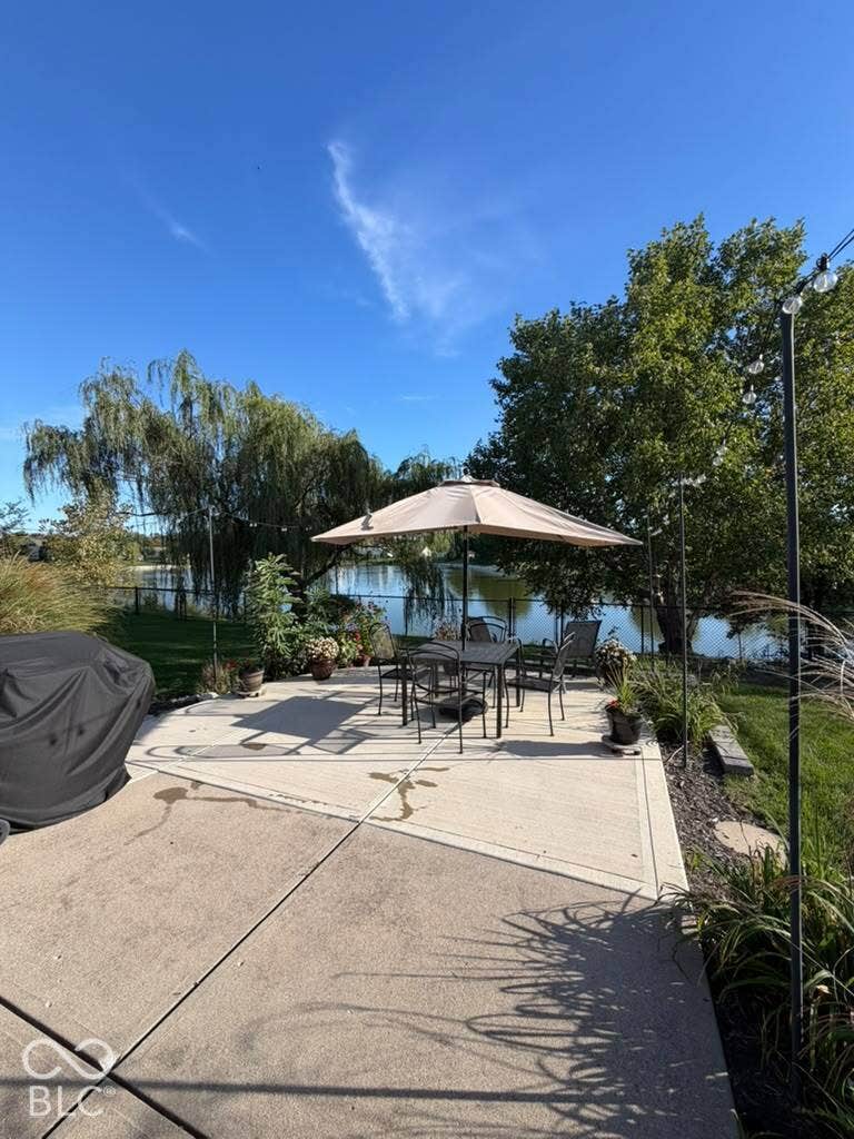 Concrete patio with a water feature backdrop, surrounded by mature trees and landscaping