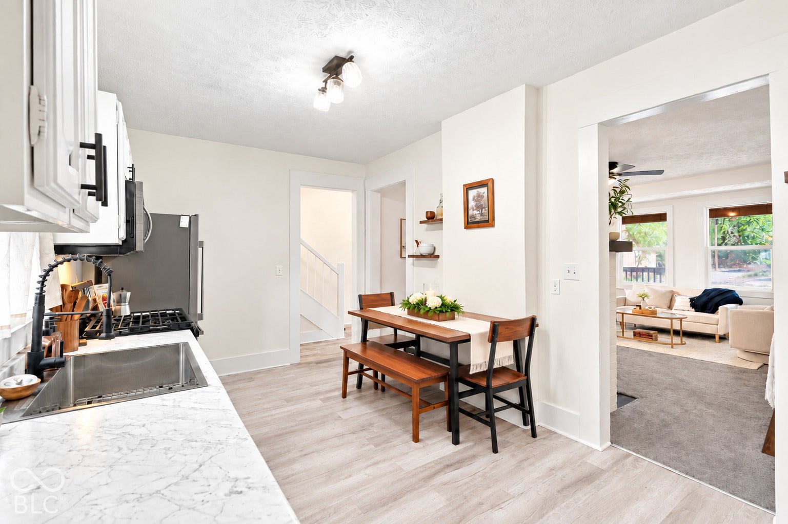 Kitchen featuring stone-patterned countertops, a stainless steel undermount sink with a matte black pull-down faucet, white cabinetry with matte black hardware, and light wood-finish flooring