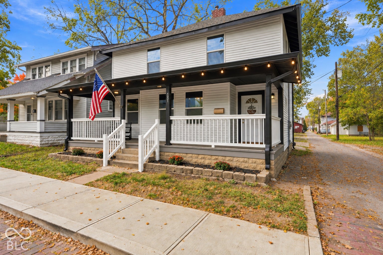 Two-story exterior featuring white horizontal siding, a covered front porch with white railing, and a masonry foundation base