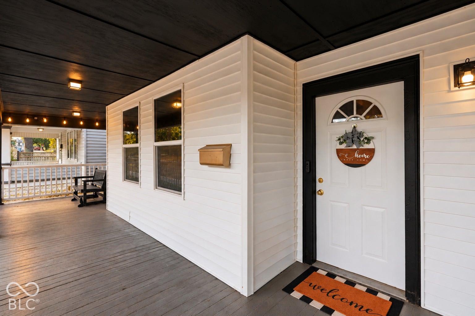 Covered front porch featuring wood finished flooring, contrasting trim, and exterior lighting.
