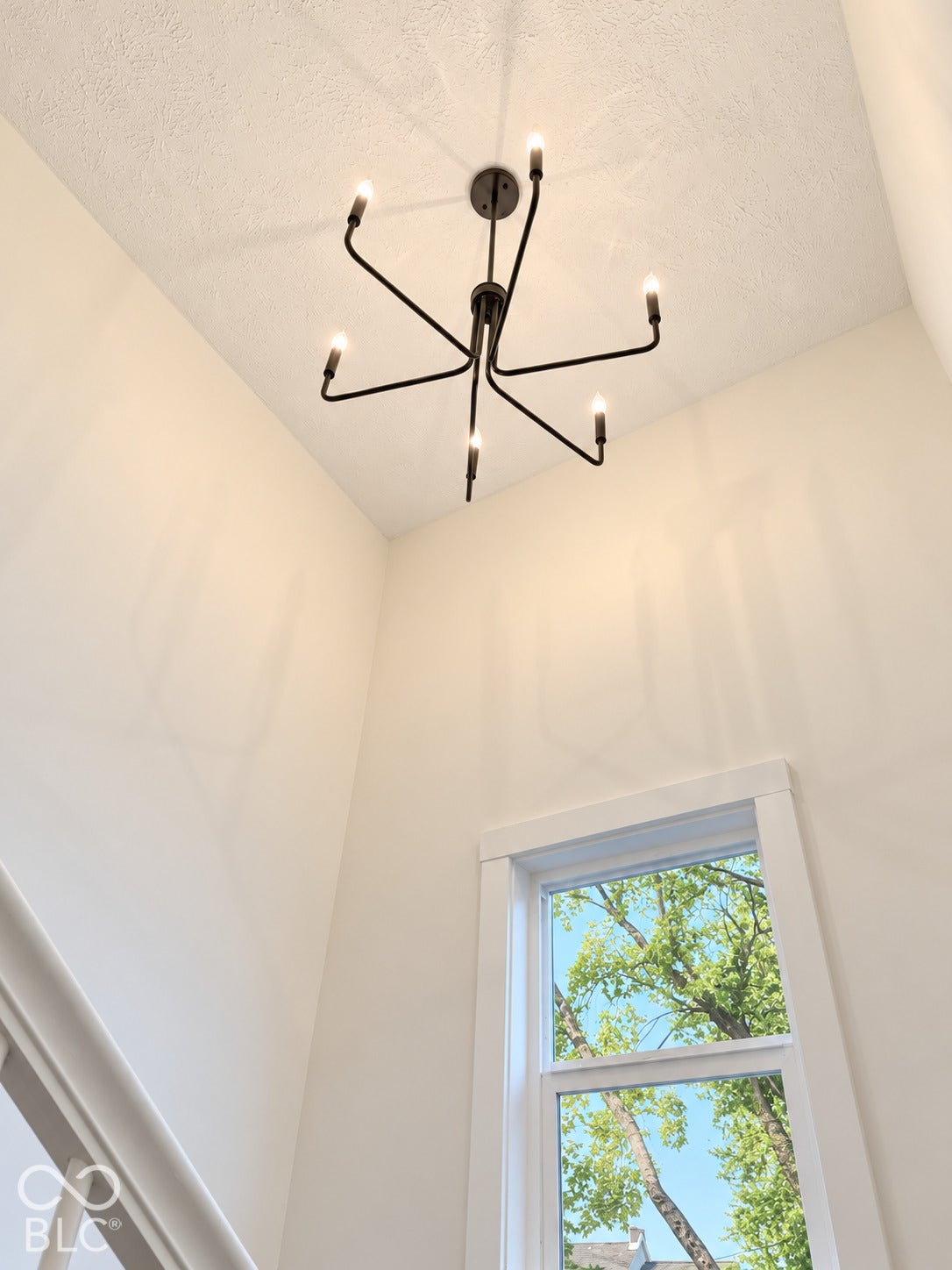 Six-arm matte black chandelier, high ceilings, and vertical window with white trim