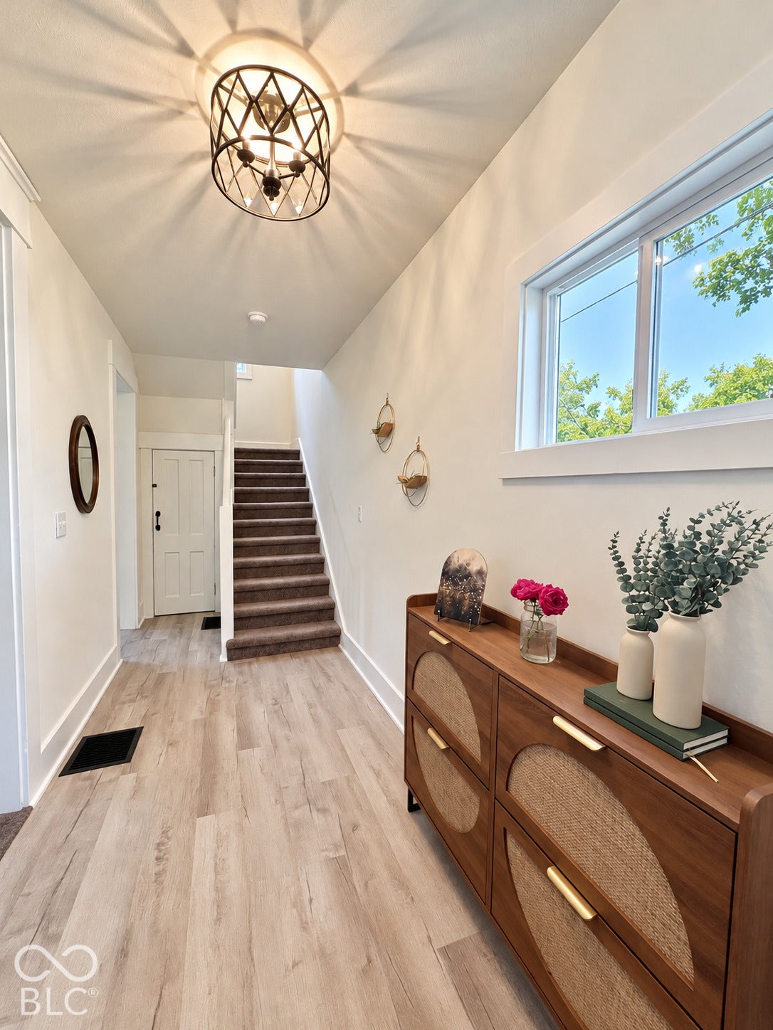 Entryway featuring light-toned wood-finish flooring, a geometric metal drum light fixture, wide-casing windows, and a carpeted staircase