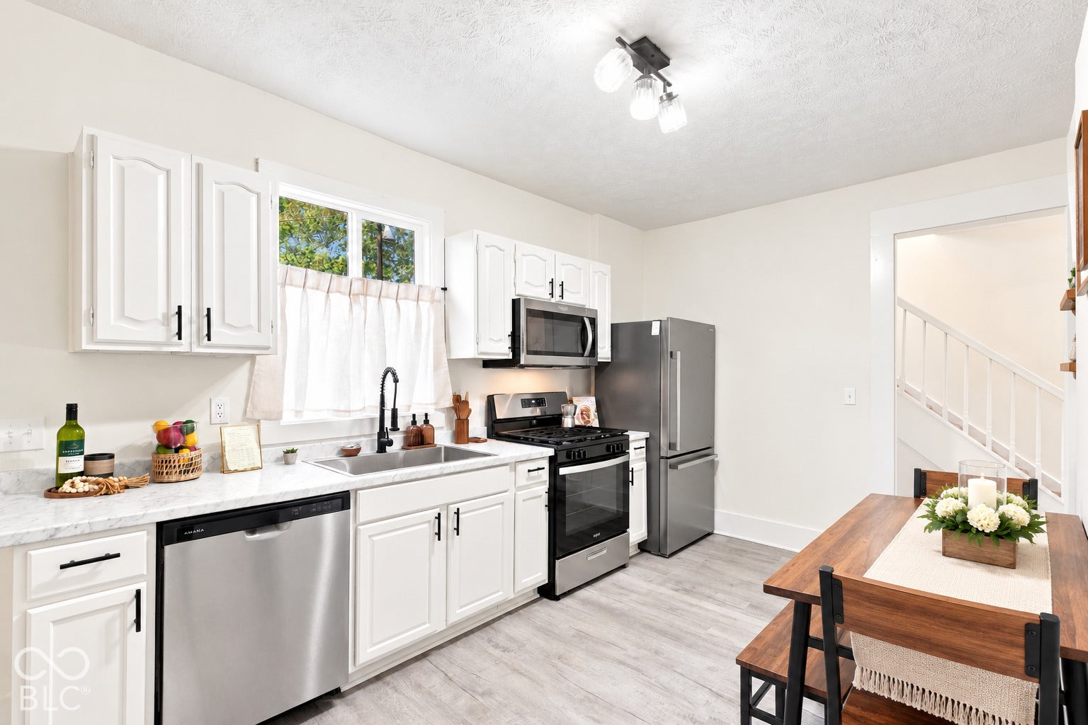 Fully updated kitchen featuring all new appliances, cabinetry, stainless steel appliances, patterned stone-finish countertops, a matte black high-arch faucet, and wood-finish flooring