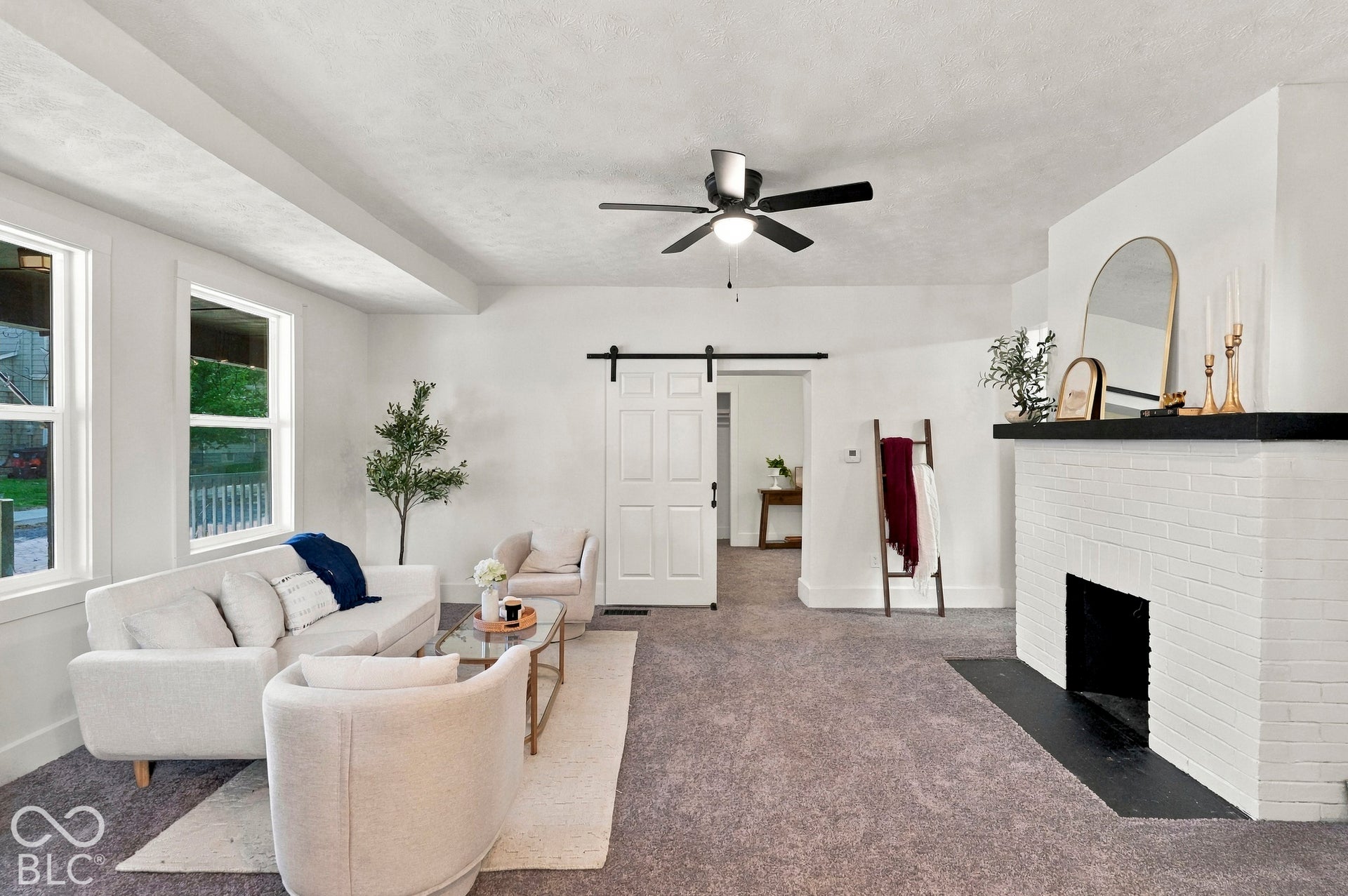 Painted brick fireplace with a contrasting mantel, sliding barn-style door, multi-pane windows, and a ceiling-mounted fan