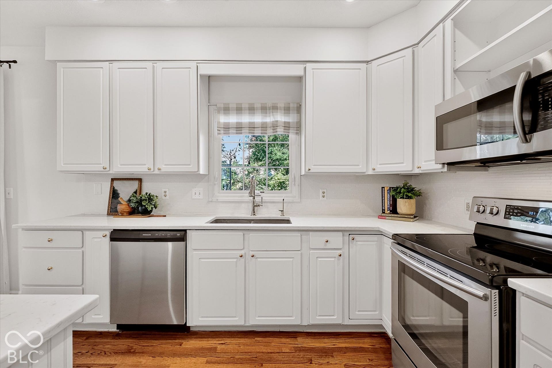 White cabinetry with gold-tone hardware, white countertops, stainless steel appliances, and wood-finish flooring