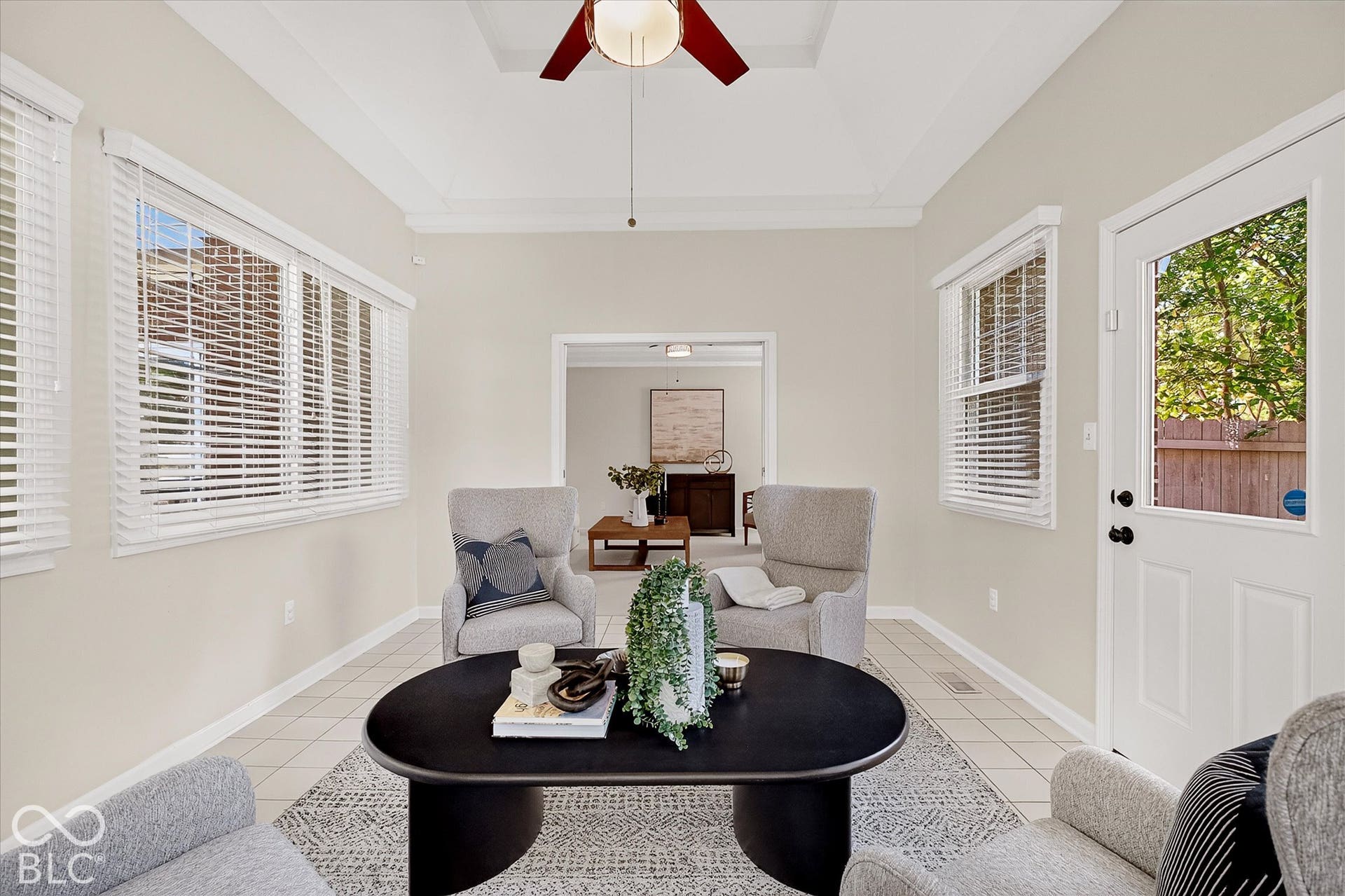 Recessed tray ceiling with crown molding, ceiling fan, multiple windows with blinds, white paneled door, and tile flooring