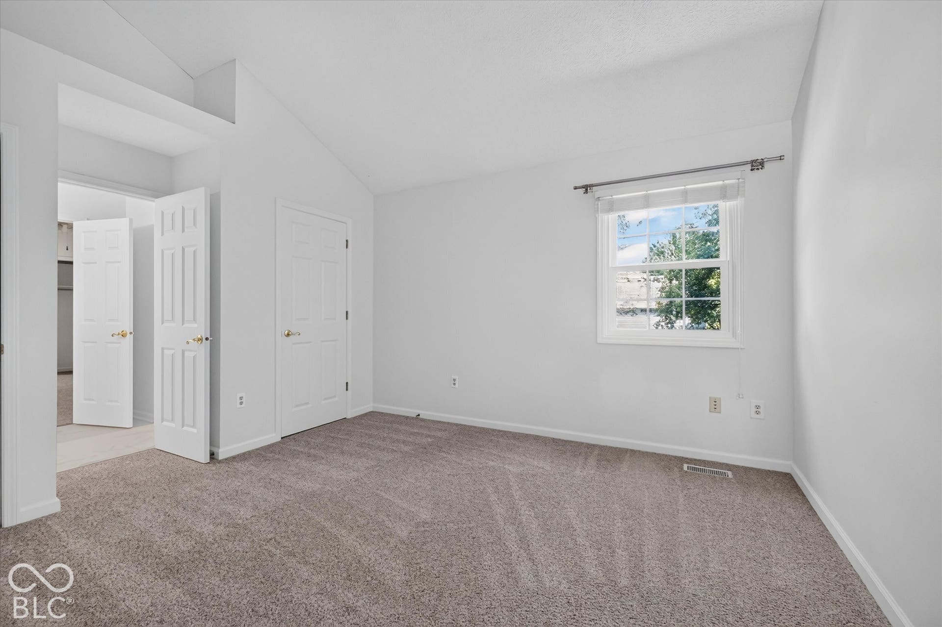 Vaulted ceiling, neutral carpeting, white trim, and a white framed window