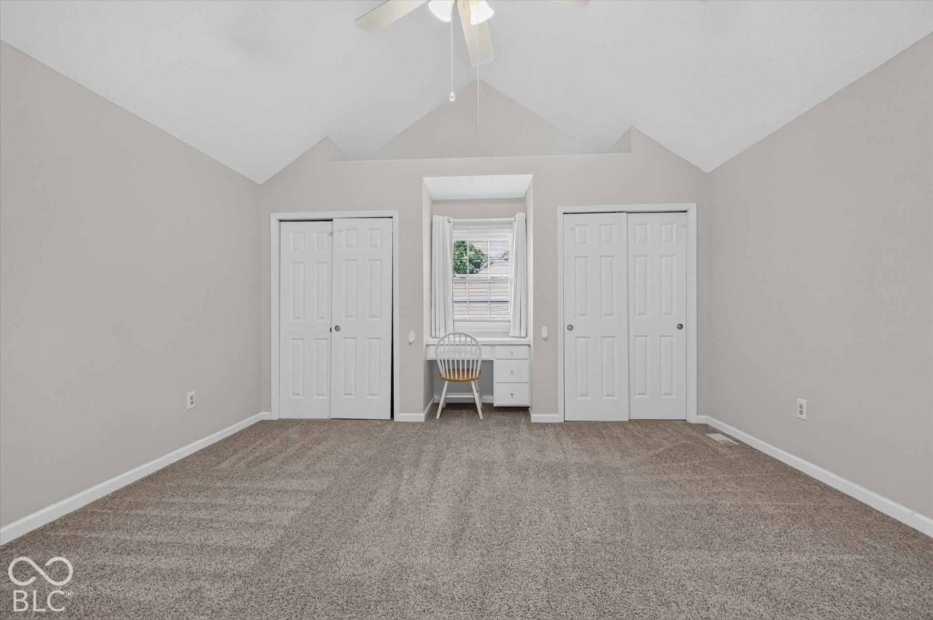 Vaulted ceiling with ceiling fan, built-in desk area, and two white bi-fold closet doors