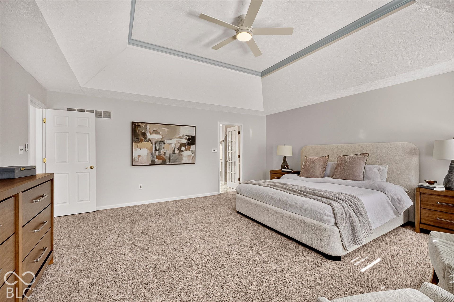 Vaulted ceiling with a central ceiling fan, tray ceiling with accent trim, light-toned carpeting, and a white paneled door