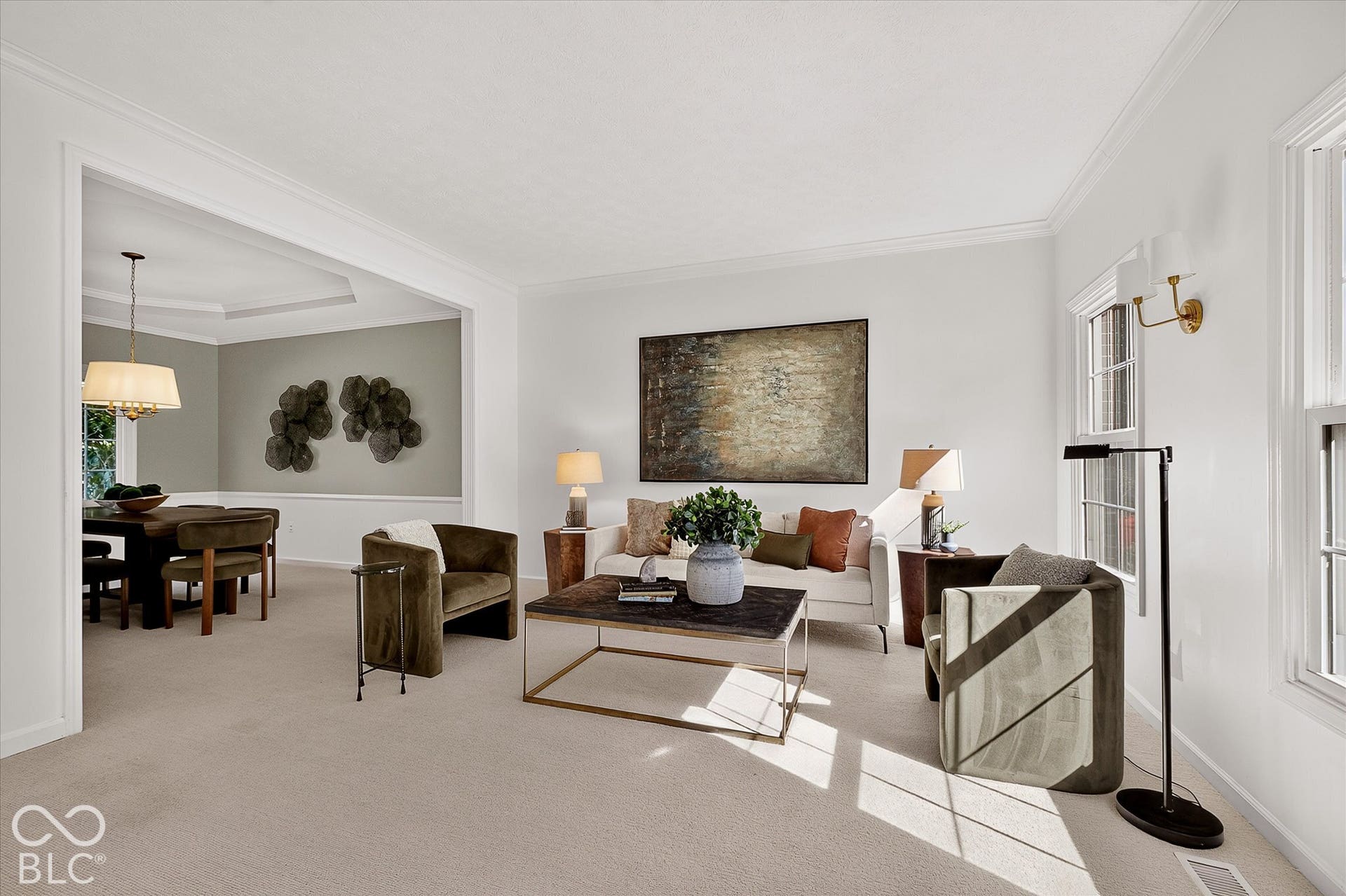 Open-concept living space with crown molding, natural light from multiple windows, and a cased opening leading to a separate dining area