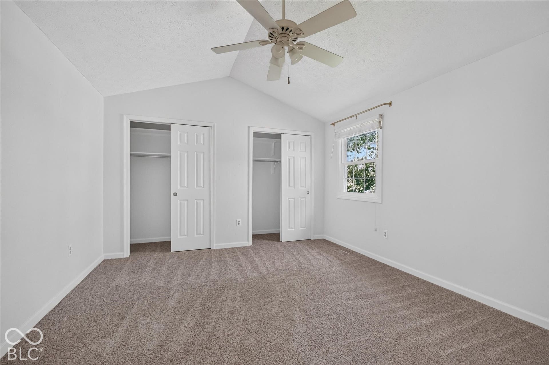 Vaulted ceiling with an attached ceiling fan, two closet spaces with bi-fold doors, and a double-hung window