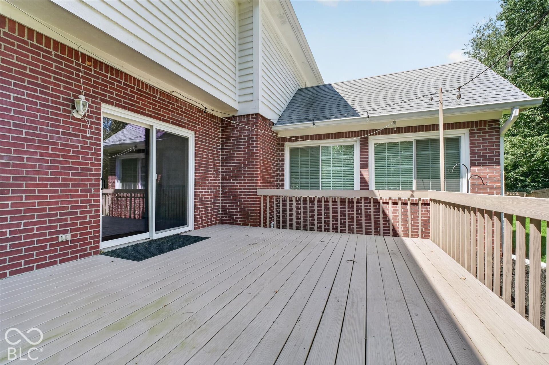 Expansive outdoor deck with wood-finish railing, red brick exterior, white siding, and multiple sliding glass doors