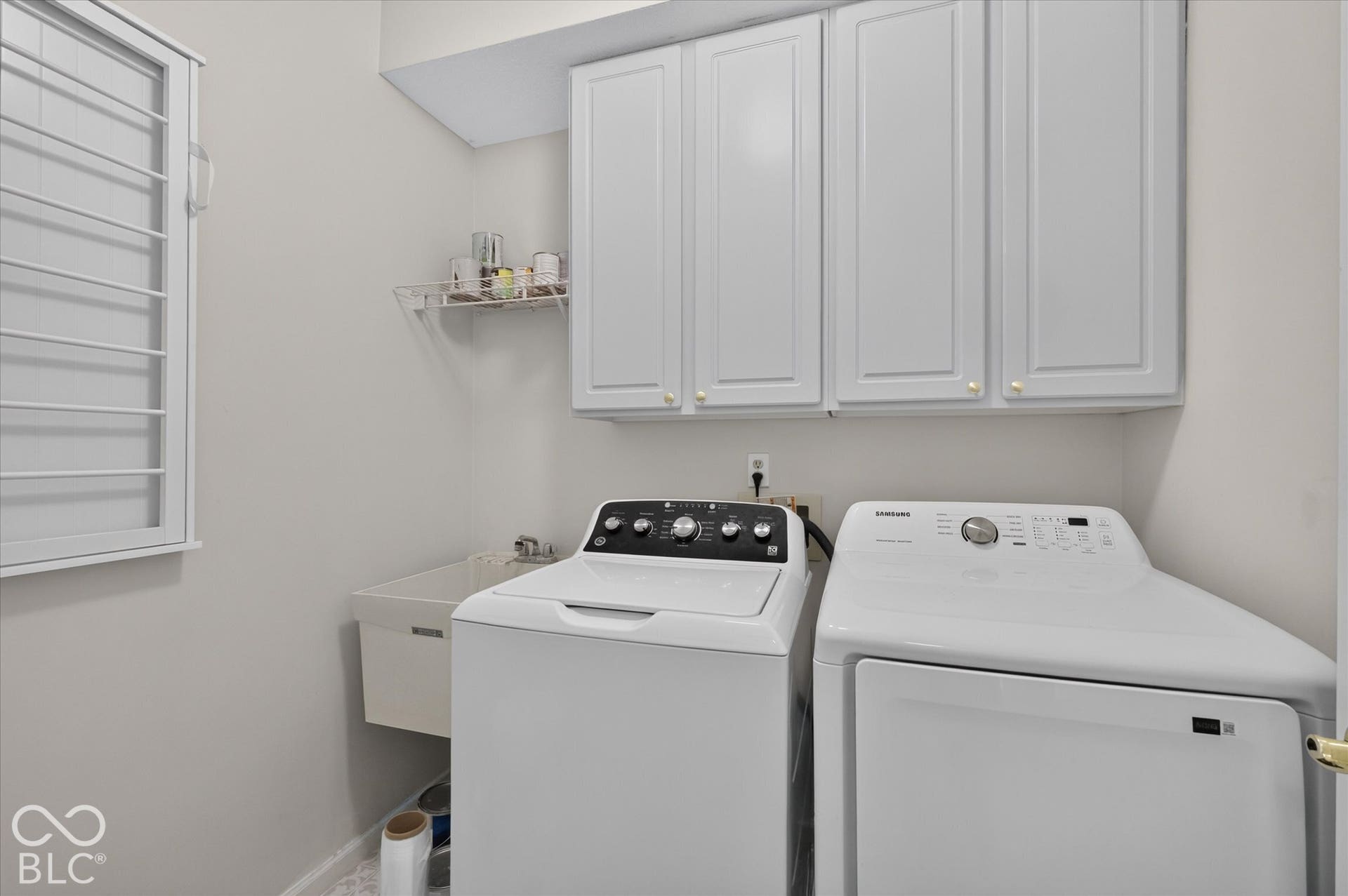 White shaker-style upper cabinetry, utility sink, wire shelving, and shutter-style window