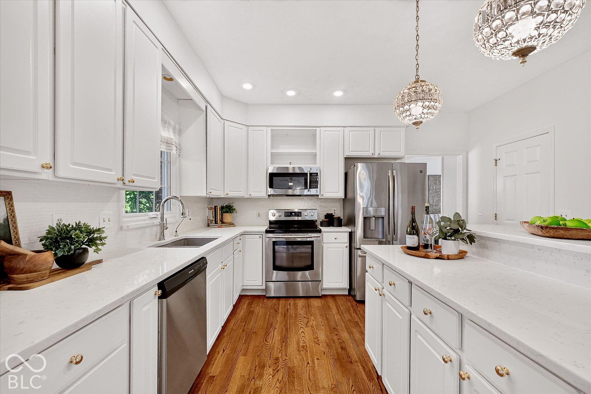 White cabinetry with gold-tone hardware, stainless steel appliances, wood-finish flooring, and white countertops