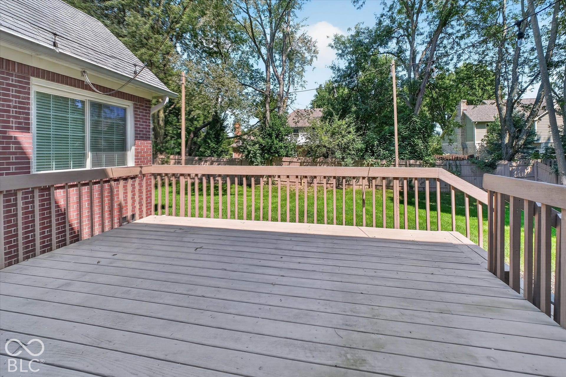 Exterior deck with wooden railings, brick-clad siding, and a visible green lawn
