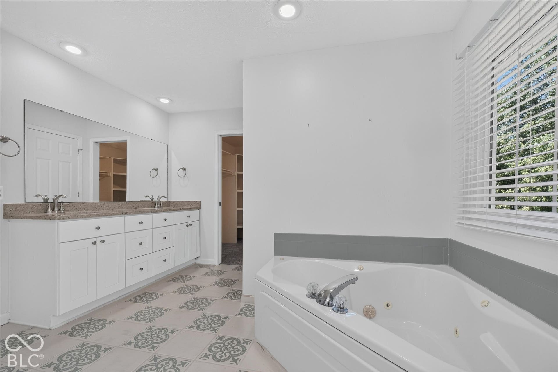 Dual vanity with integrated sinks, corner jetted tub, patterned floor tile, and recessed lighting