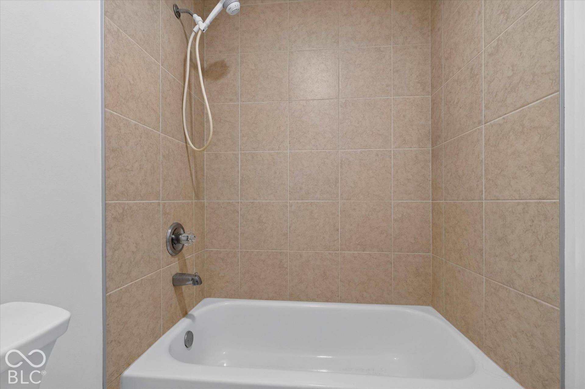 White bathtub with a chrome faucet and showerhead, surrounded by beige tile walls