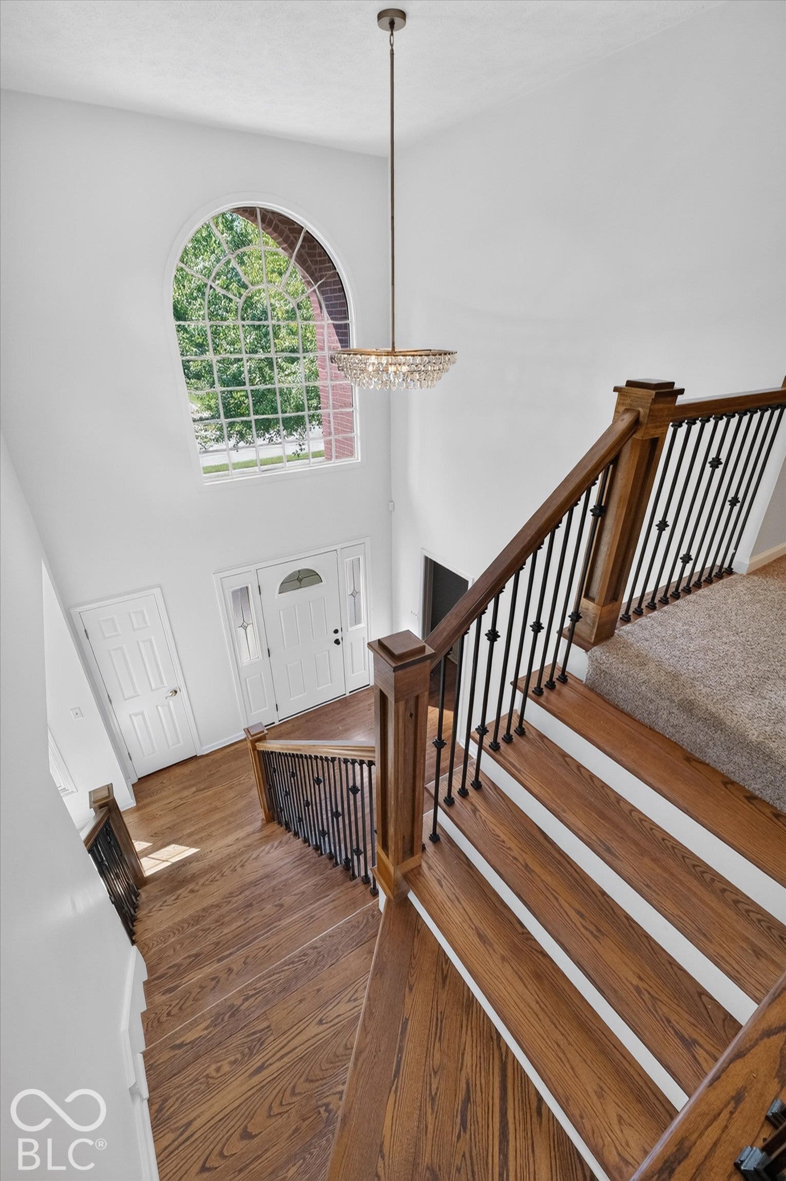 Two-story foyer with a large arched window, a decorative chandelier, and hardwood flooring