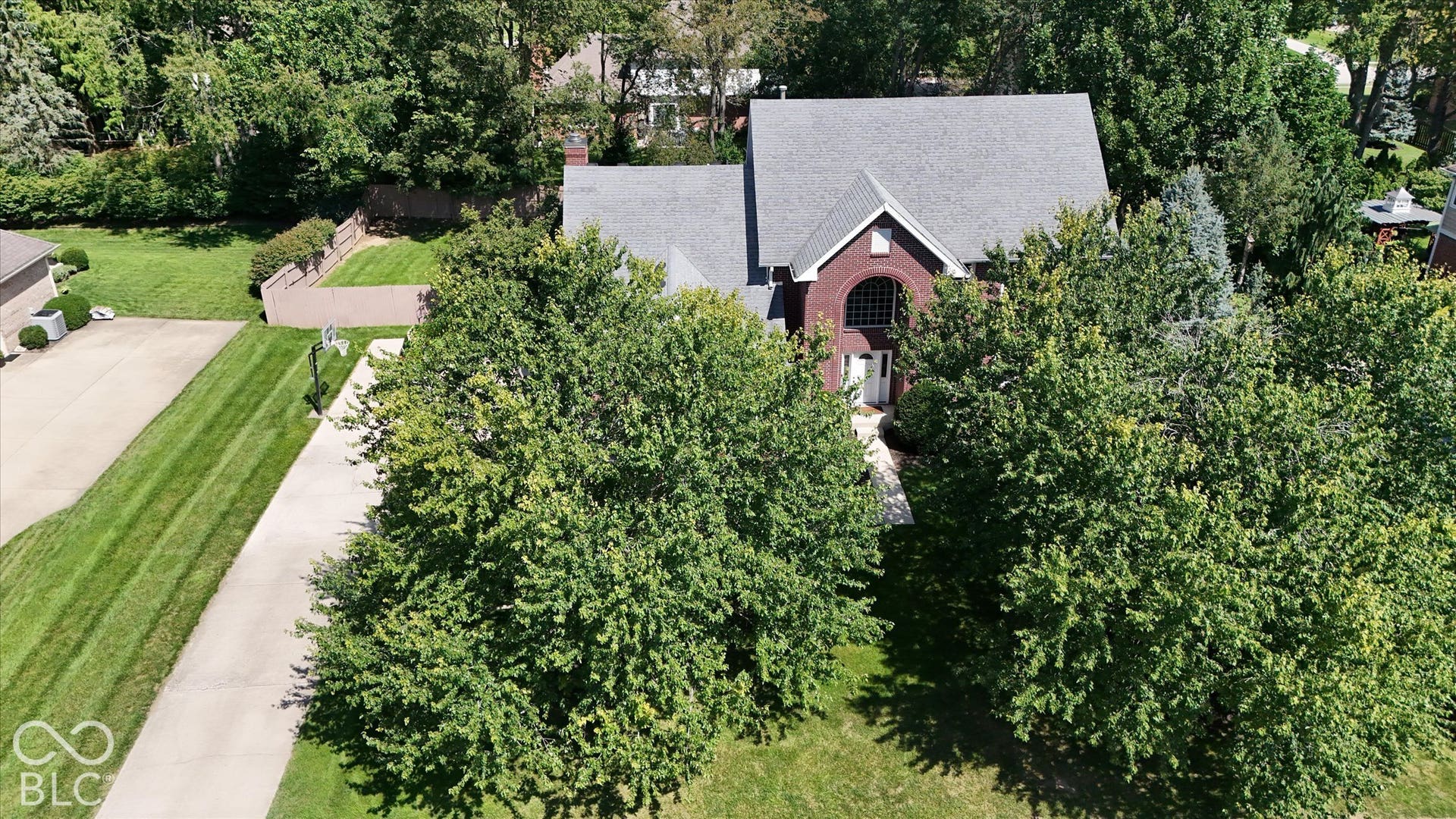 Red brick exterior with a prominent arched window, gabled roofline, mature trees, and a concrete driveway